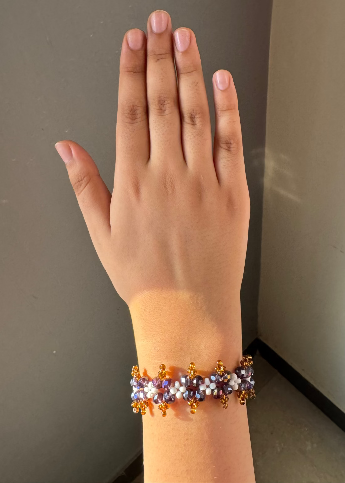 Hand wearing a beaded bracelet against a neutral background