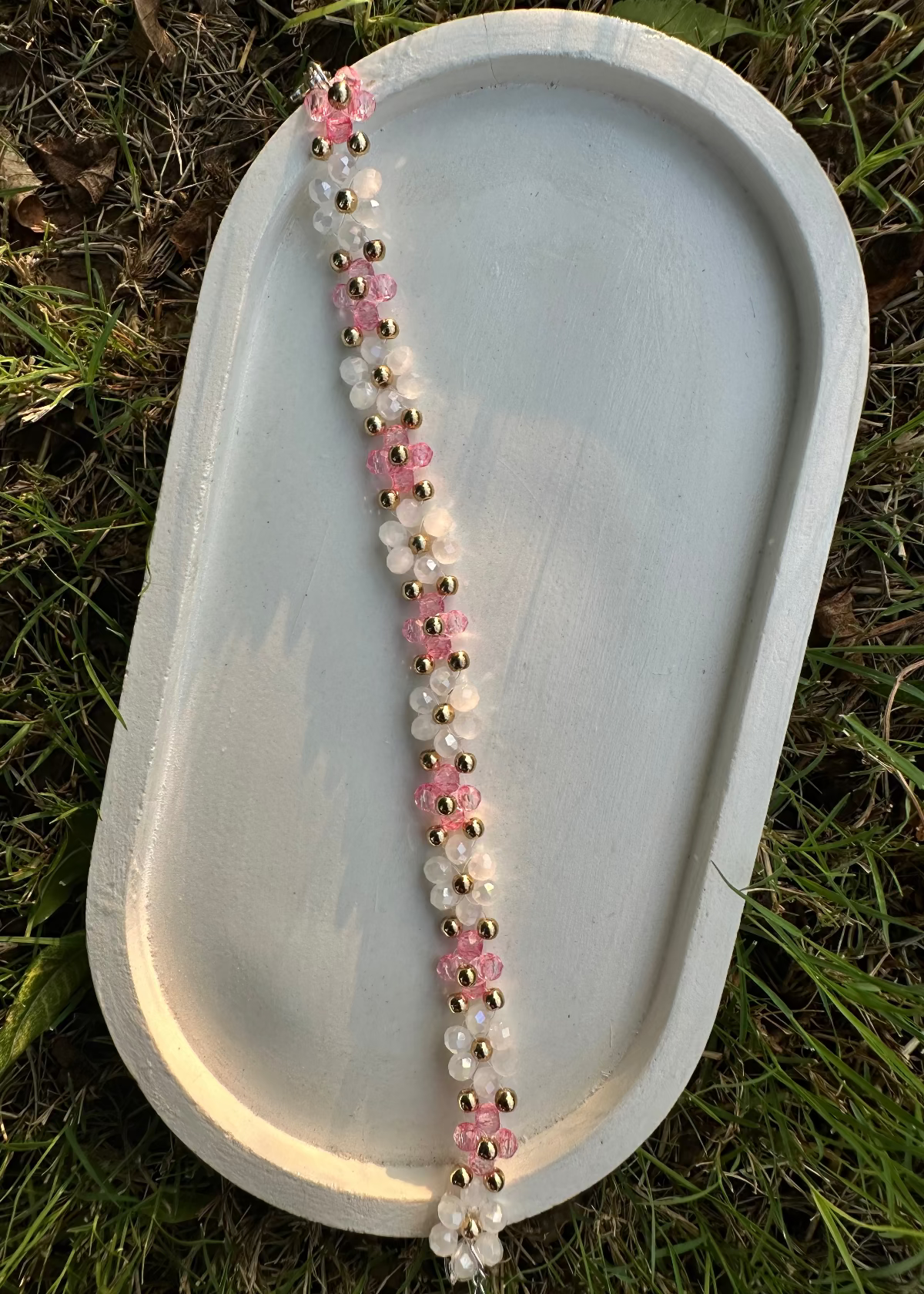 Beaded necklace with pink and white beads on a stone surface outdoors