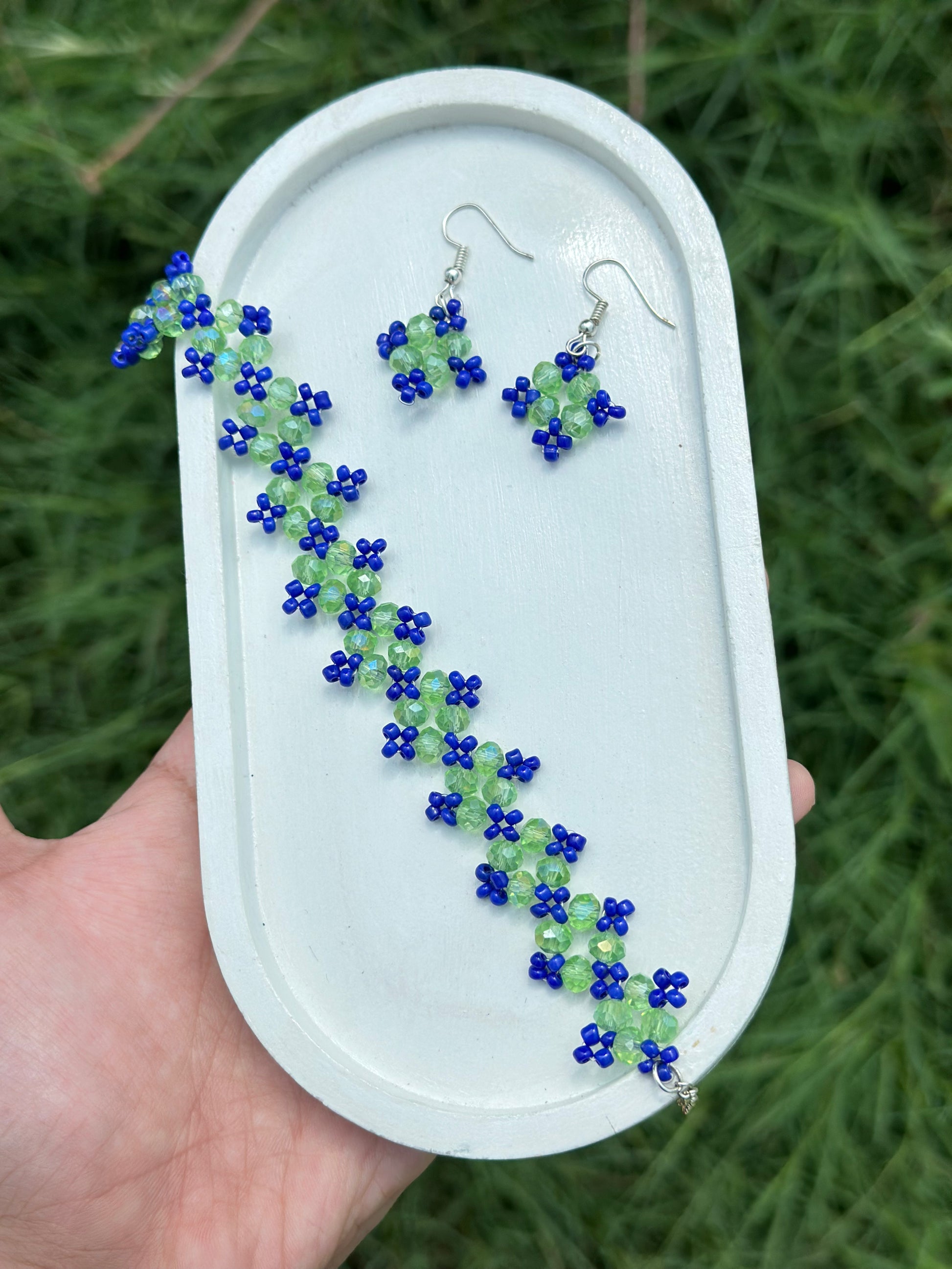 Beaded earrings on a white display card held by a hand with a green leafy background