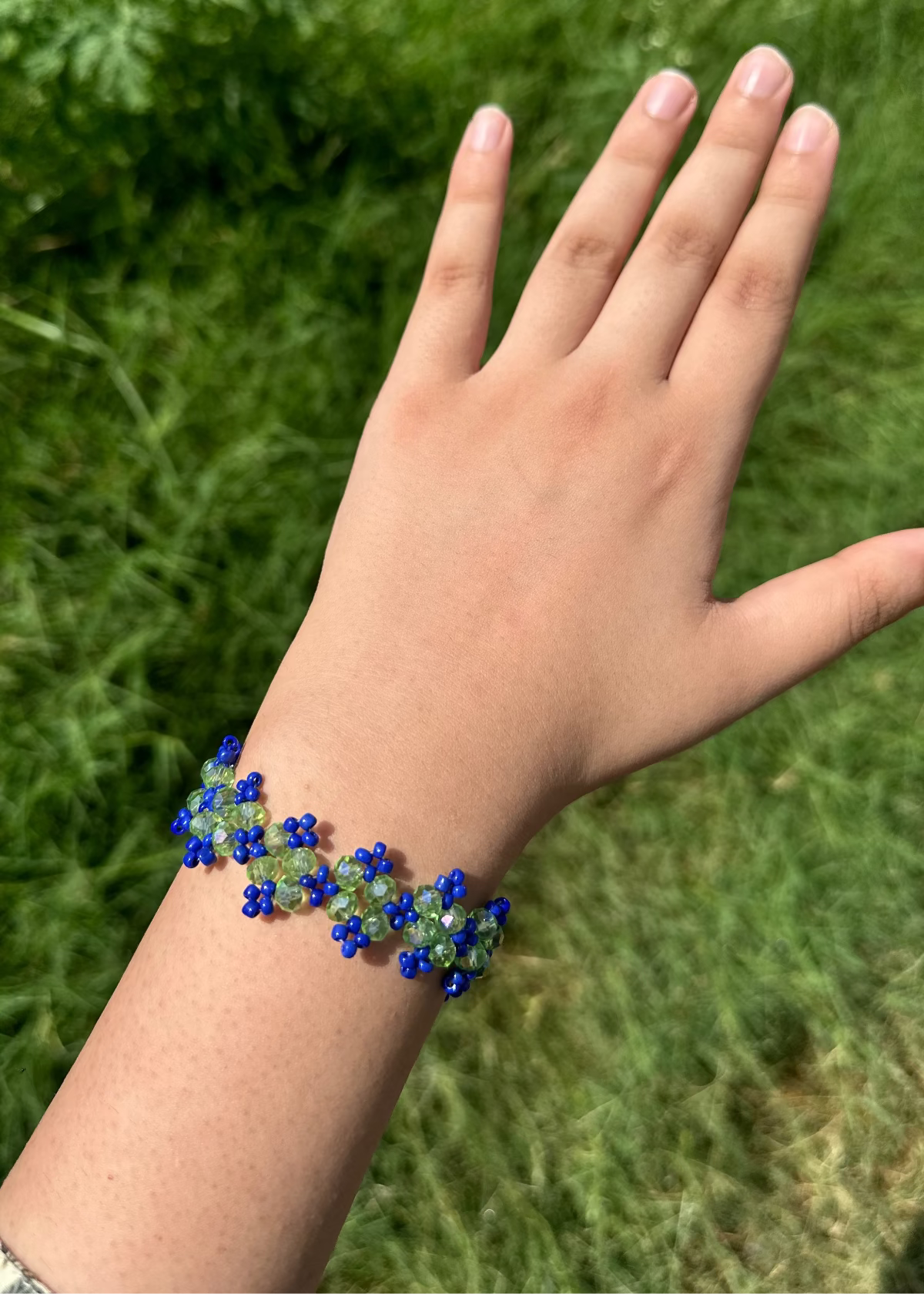 Hand wearing a blue beaded bracelet against a grassy background