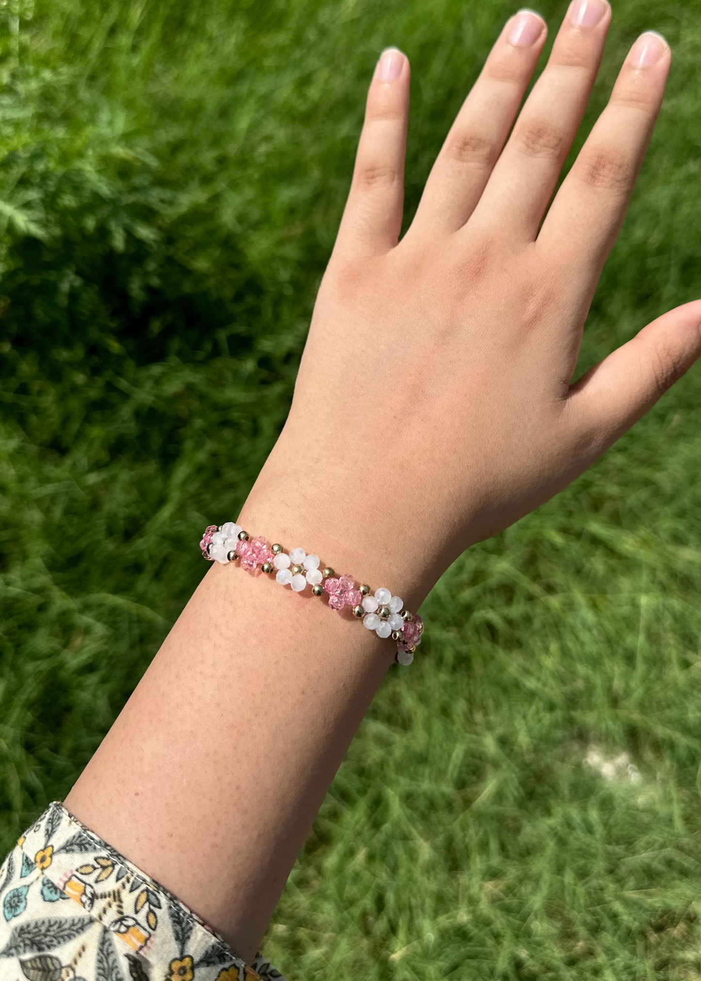 Hand wearing a pink floral bracelet against a grassy background