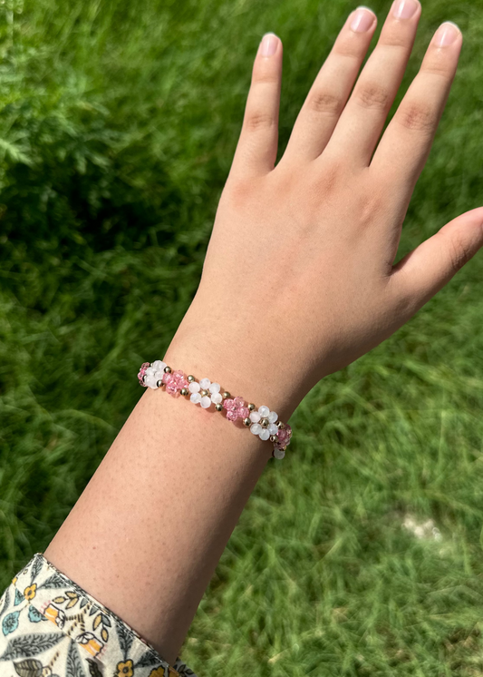Hand wearing a pink floral bracelet against a grassy background