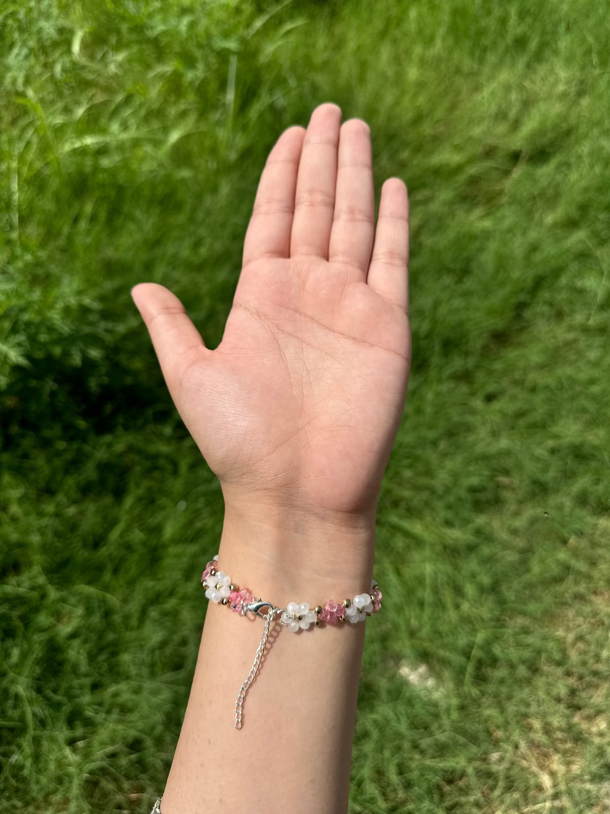 Hand wearing a bracelet against a grassy background
