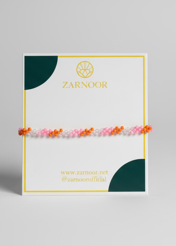 Hand holding a Zarnoor branded card with a bracelet on a grassy background