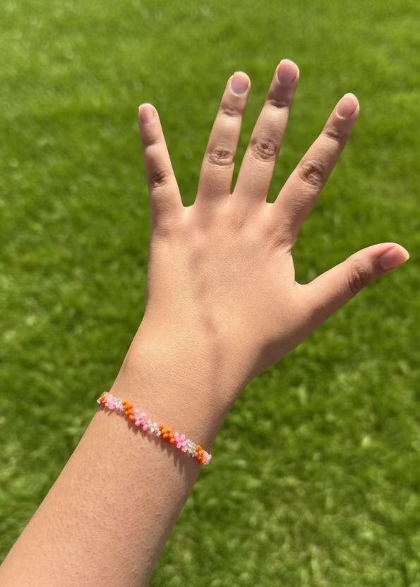 Hand with a colorful beaded bracelet against a grassy background