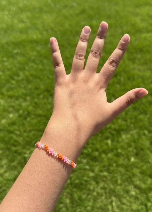 Hand with a colorful beaded bracelet against a grassy background