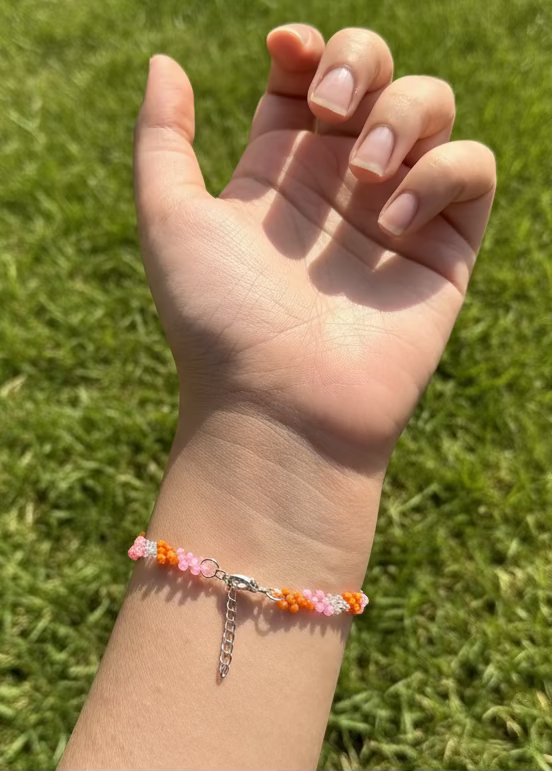 Hand wearing a colorful bracelet with grass in the background