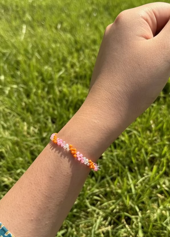 Hand wearing a colorful beaded bracelet against a grassy background