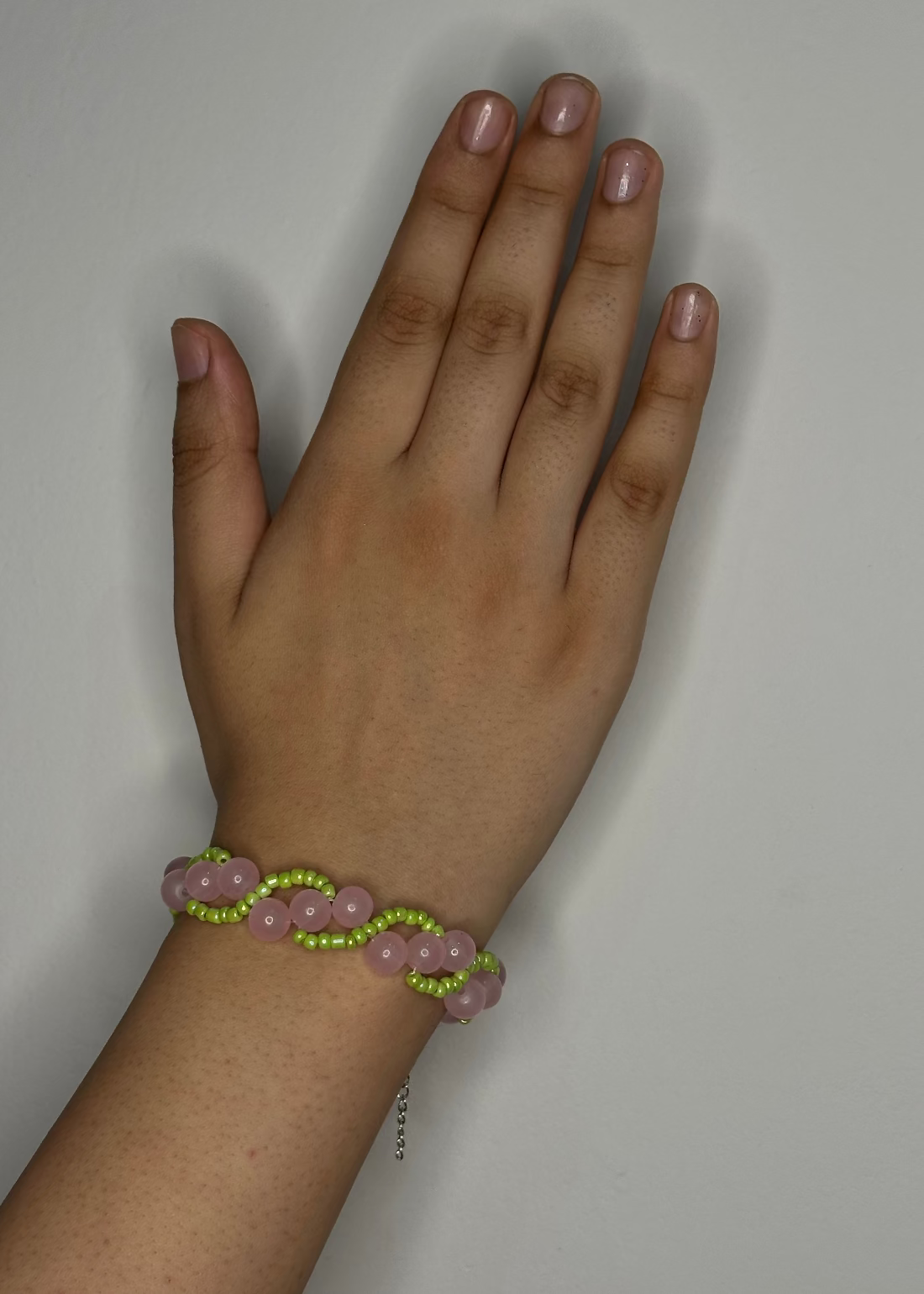 Hand wearing a bracelet with pink and green beads on a plain background