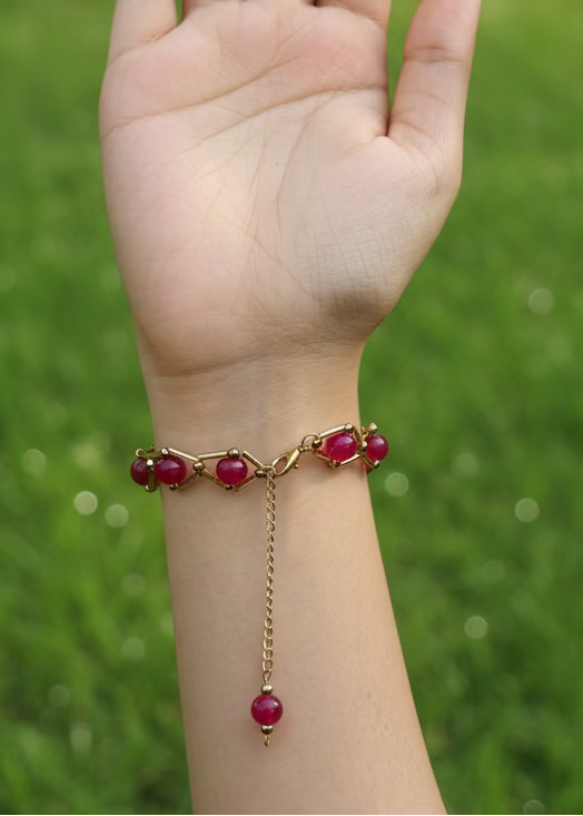 Bracelet with red beads on a wrist against a plain background