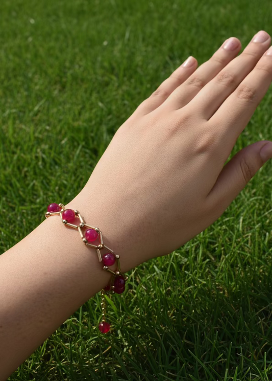 Hand wearing a bracelet with red stones on a plain background
