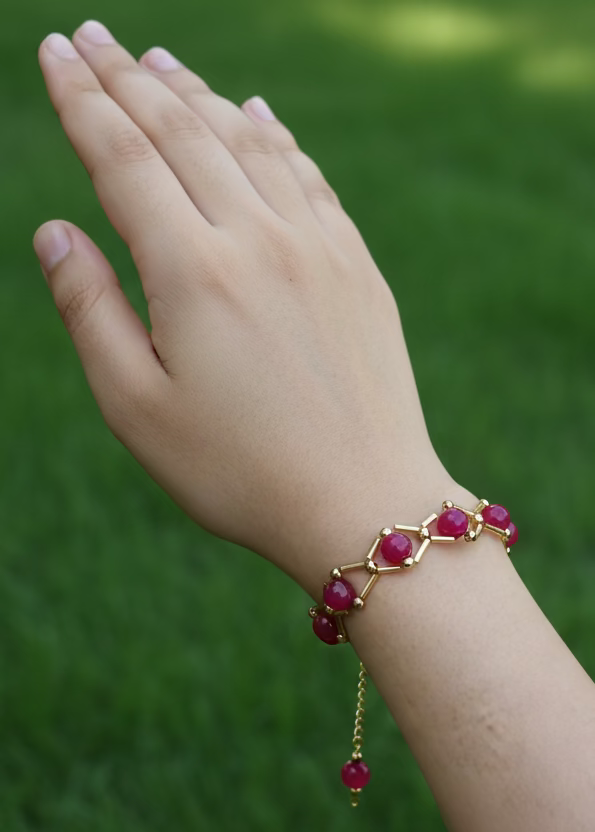 Hand wearing a red beaded bracelet on a plain background