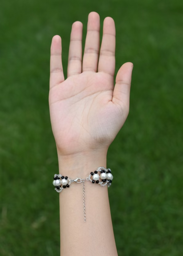 Hand wearing a bracelet with pearls against a plain background