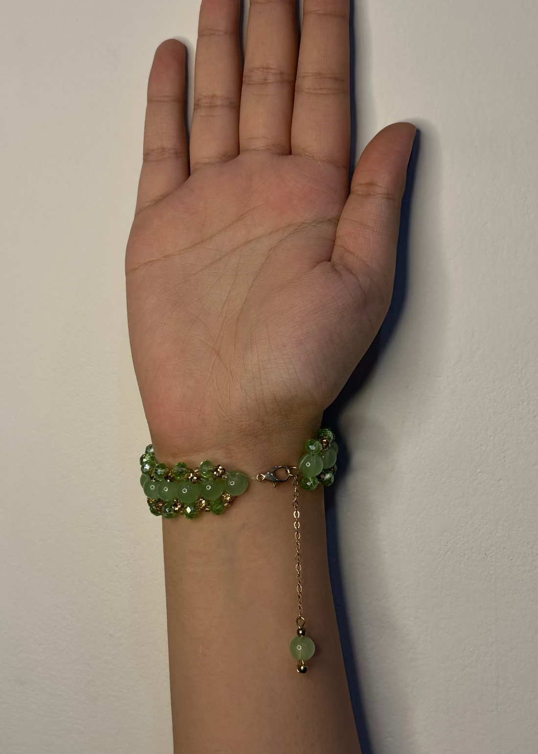Hand wearing a green beaded bracelet against a plain background