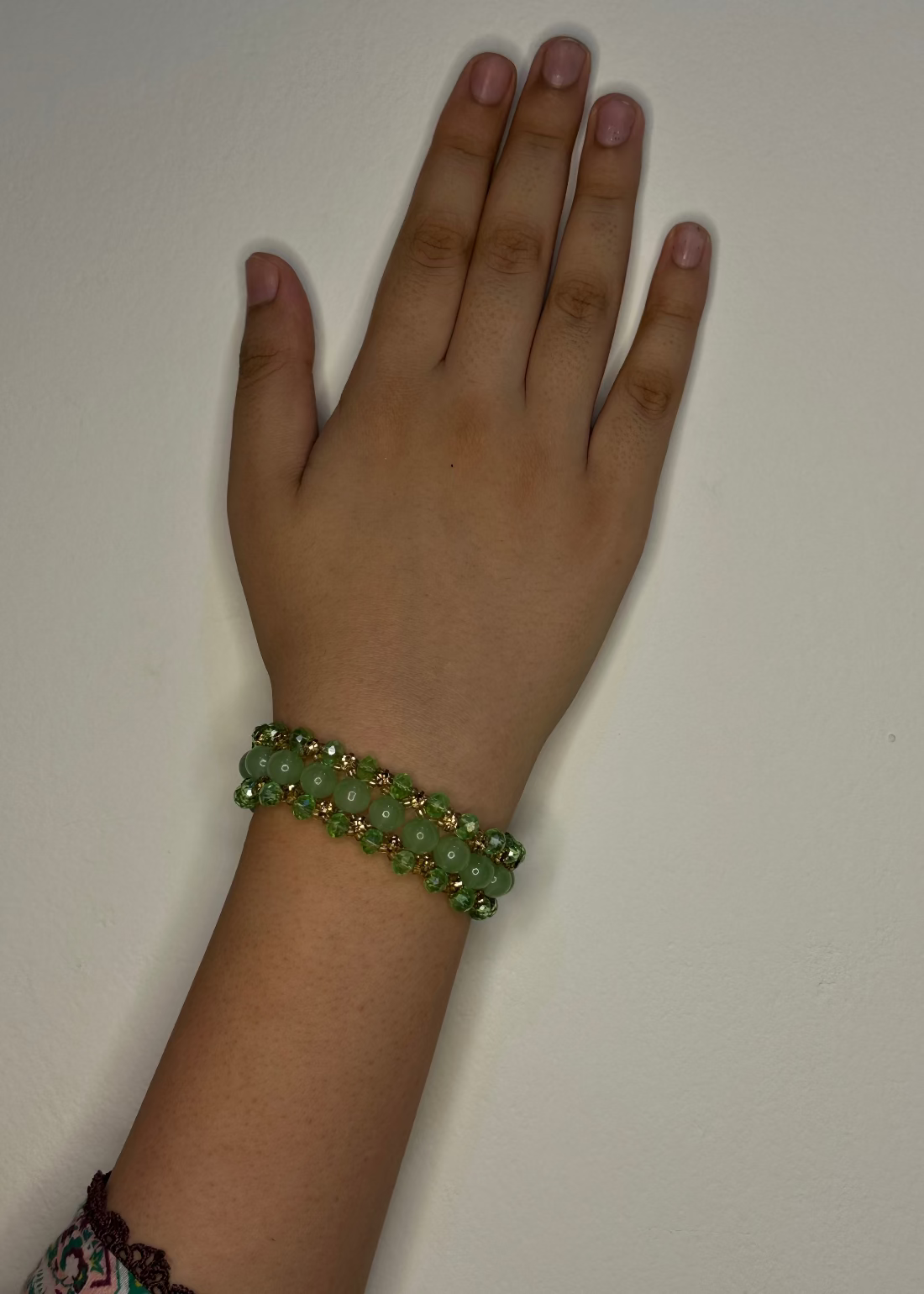 Hand wearing a green beaded bracelet on a plain background