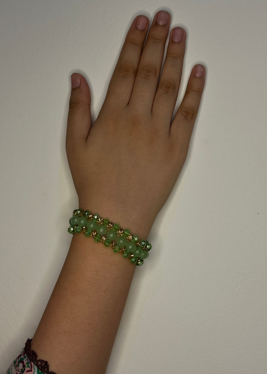 Hand wearing a green beaded bracelet on a plain background