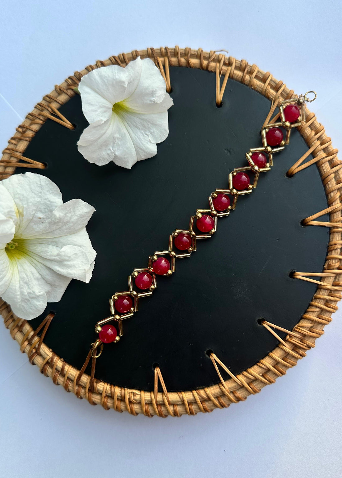 Bracelet with red gemstones on a black circular background with white flowers