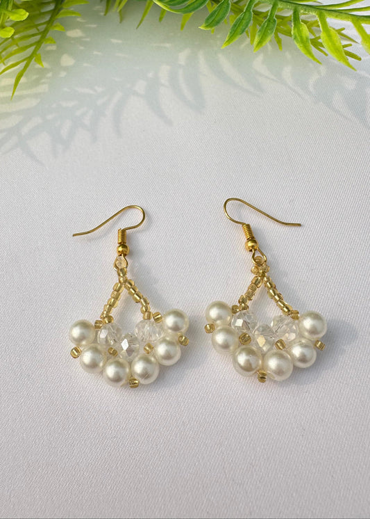 A pair of earrings featuring a triangle-shaped design with a blend of silver and golden beads, attached to a white surface with a green leaf in the background.